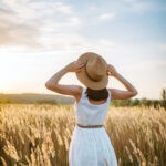 Woman in dress walking in wheat field on sunset