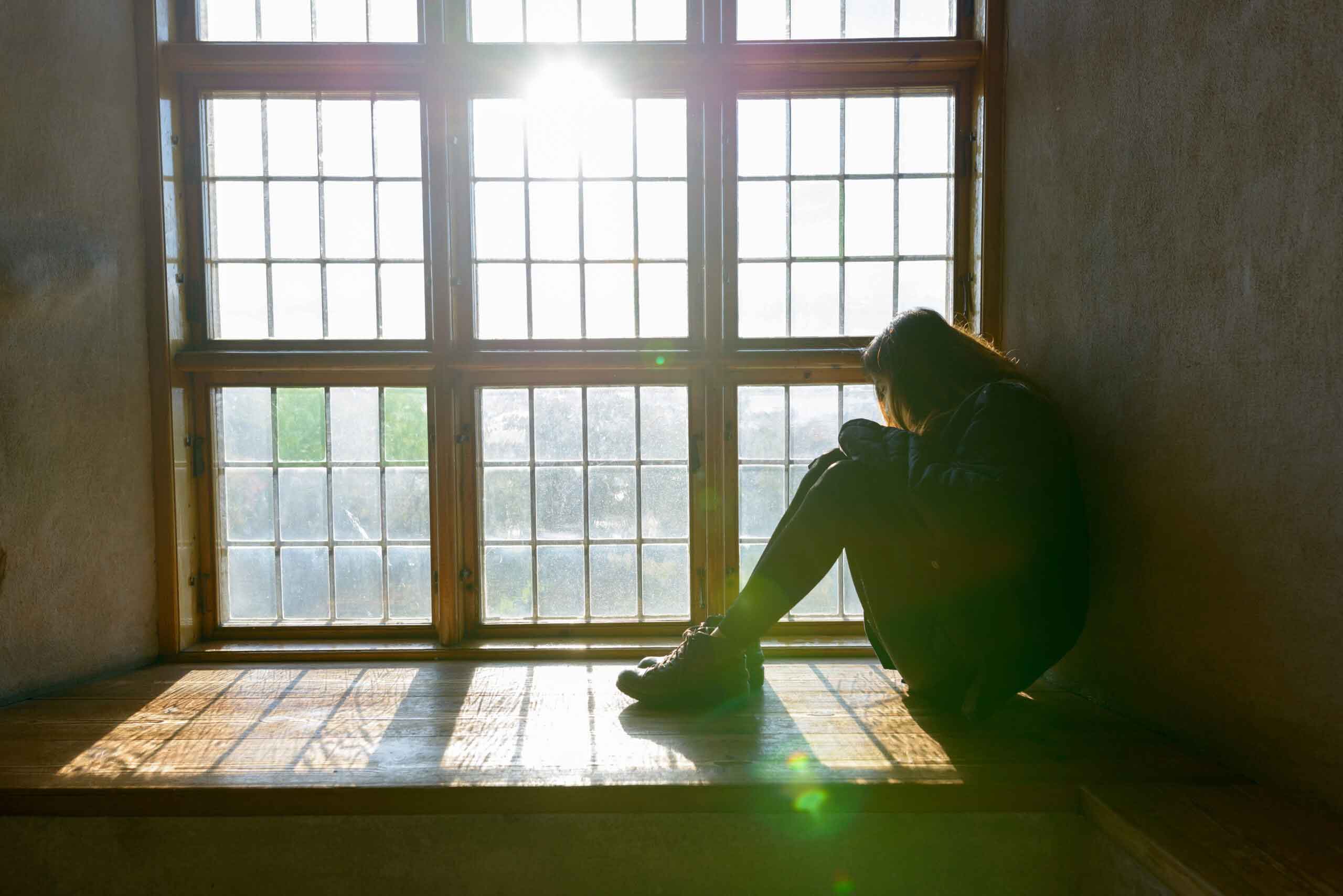 Young woman sitting in front of closed wooden window with sunlight streaming in